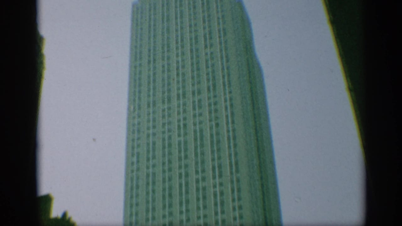 1959 New York frame showing a tall skyscraper seen from below, bordered by dark gate edges and soft color tint.