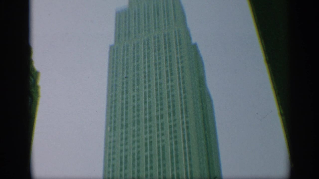 1959 New York home-movie frame showing the upper Empire State Building facade from a low angle, with dark film-edge borders.