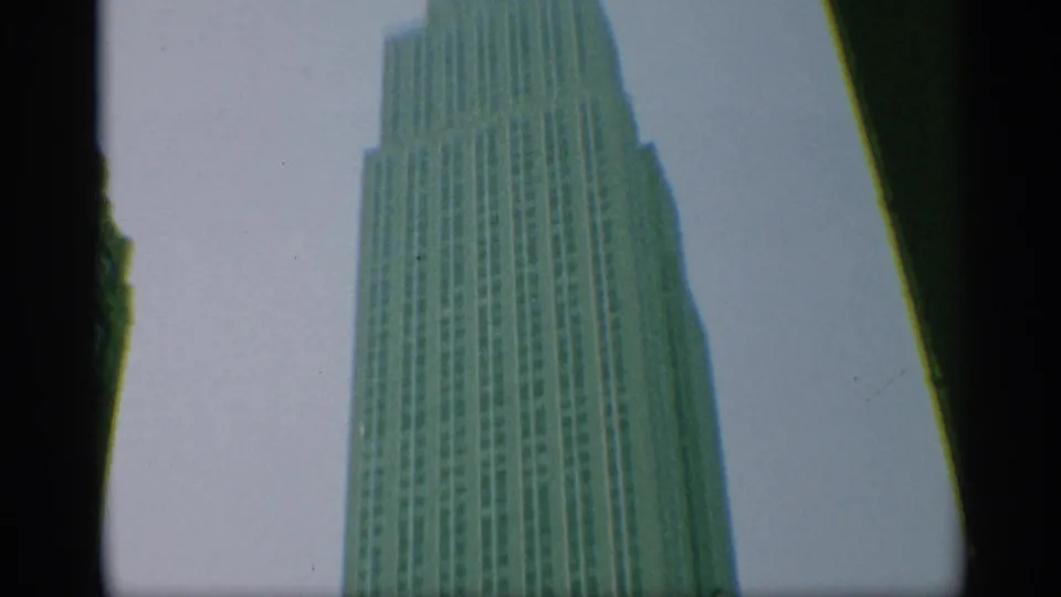1959 New York home-movie frame showing the upper Empire State Building facade from a low angle, with dark film-edge borders.
