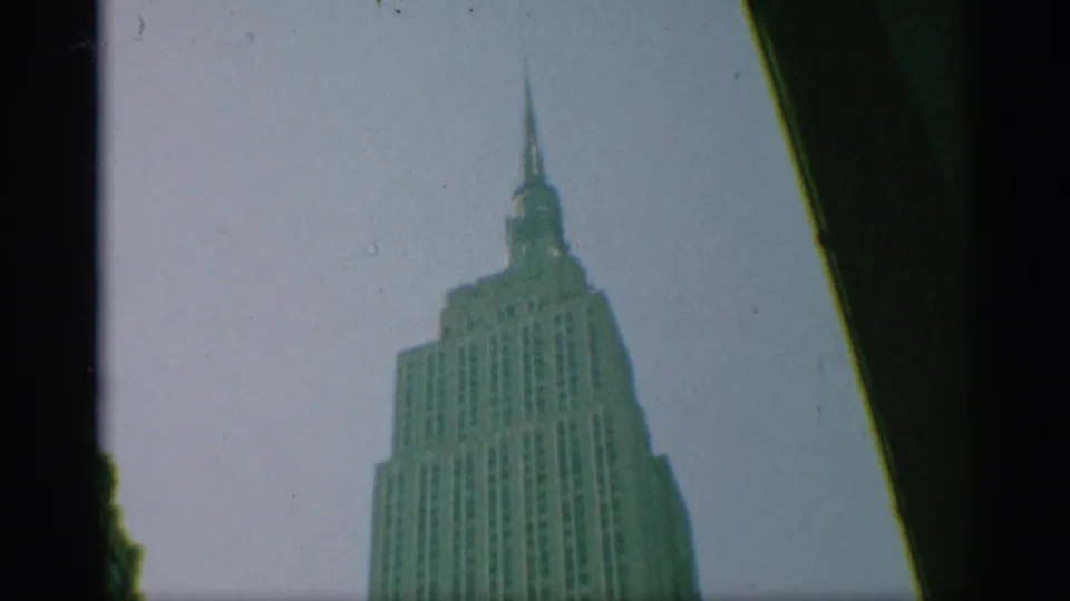 1959 New York frame of the Empire State Building upper floors and spire, seen through a soft green-tinted 8mm scan.