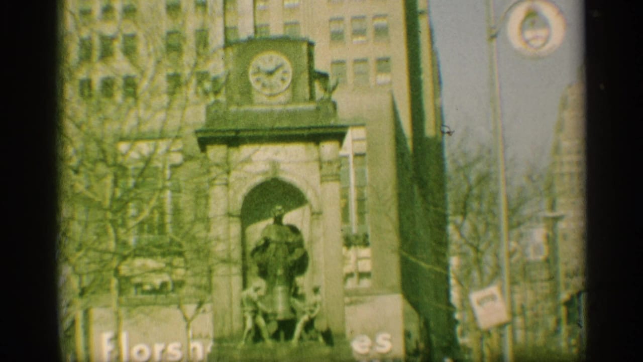 1959 New York street view of a monument-like facade with a statue under an arch, bare trees, and surrounding urban buildings.