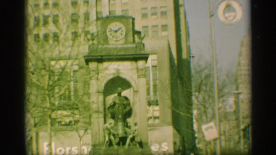 1959 New York street view of a monument-like facade with a statue under an arch, bare trees, and surrounding urban buildings.