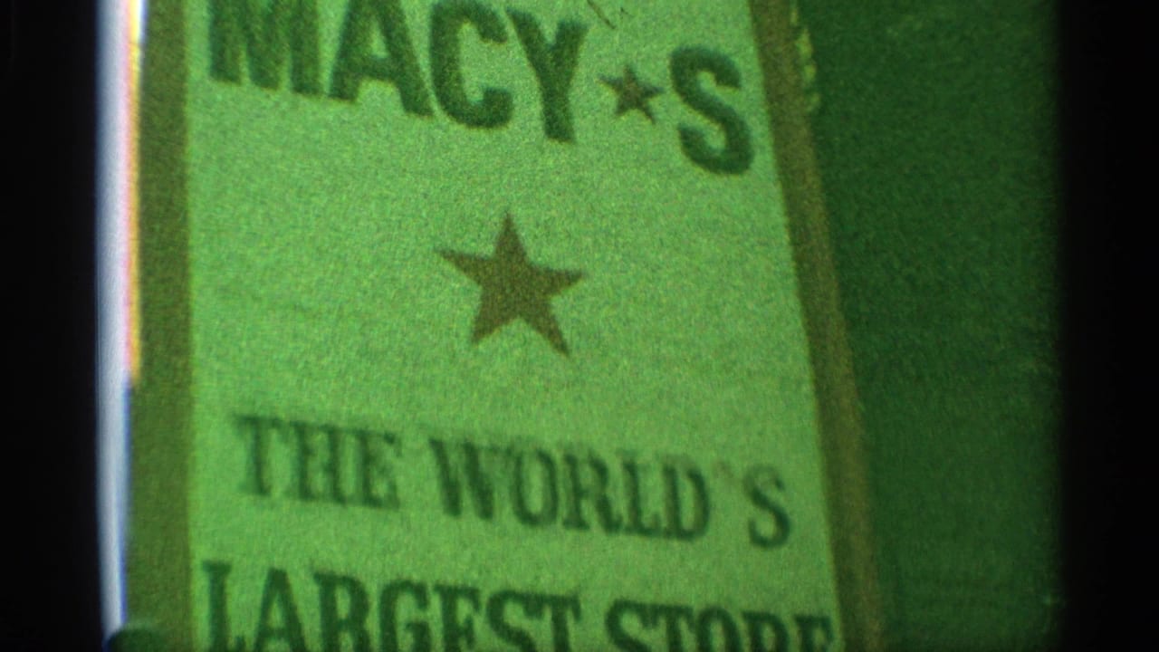 1959 New York home-movie frame showing a green Macy's sign with star emblems and partial world's-largest-store wording.