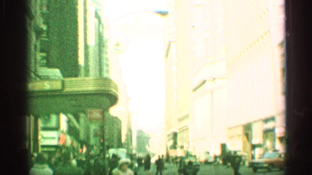 Green-tinted New York sidewalk view with pedestrians, tall buildings, and bright overexposed street light.