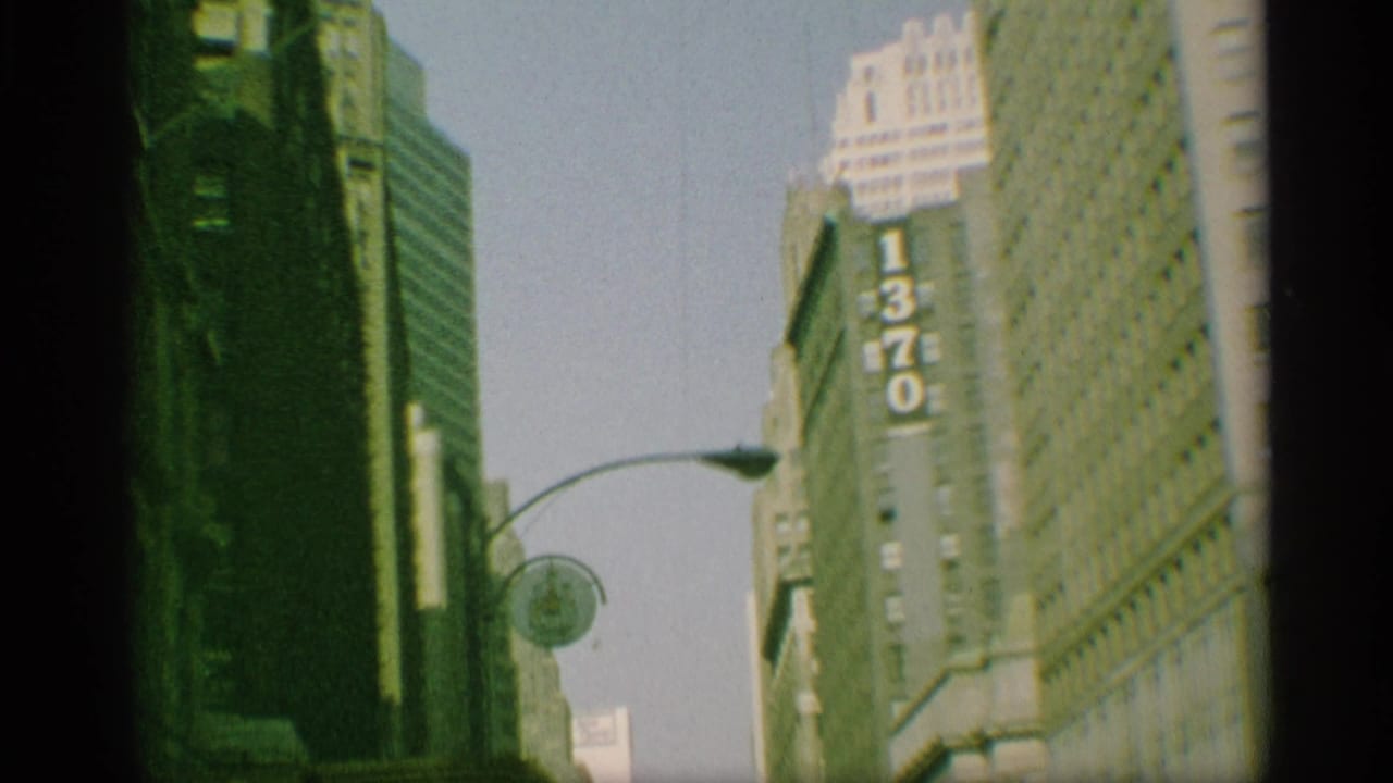 1959 New York street scene with tall buildings, a visible 1370 sign, curved street lamp, and soft color-faded 8mm texture.