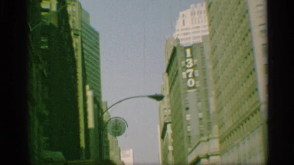 1959 New York street scene with tall buildings, a visible 1370 sign, curved street lamp, and soft color-faded 8mm texture.