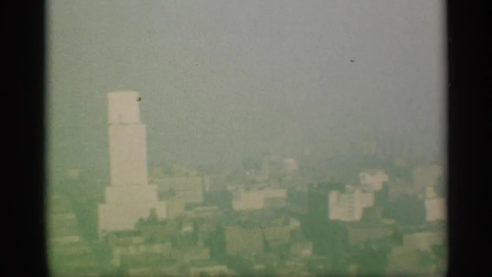 Color-faded 8mm skyline view in New York, showing a pale tower form and distant buildings through haze or smog.