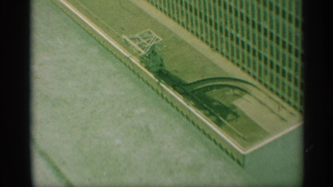 Home-movie frame showing an angled New York building facade and nearby water or flooded ground in soft 8mm color.