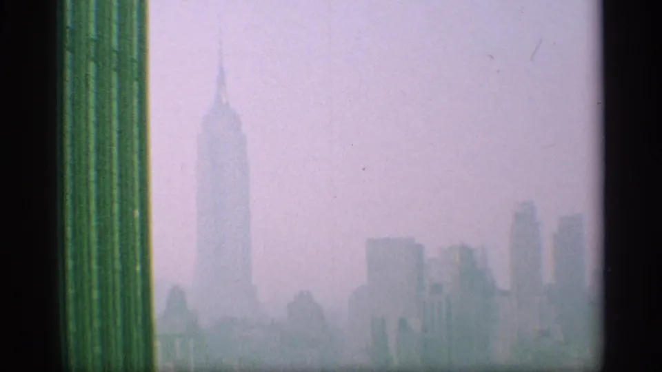 Hazy 1959 New York skyline seen through a window or frame edge, with the Empire State Building rising above surrounding buildings.