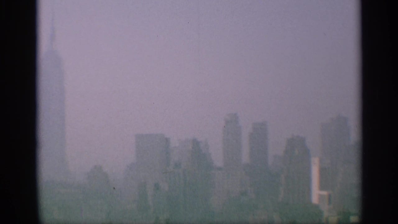 1959 New York 8mm skyline frame showing soft silhouettes of Manhattan high-rises under a pale, hazy sky.
