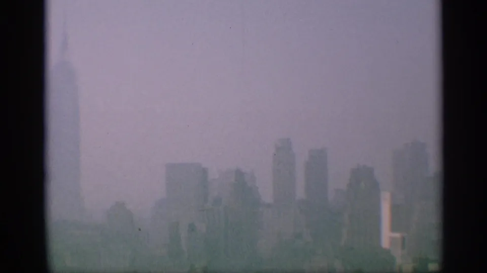 1959 New York 8mm skyline frame showing soft silhouettes of Manhattan high-rises under a pale, hazy sky.