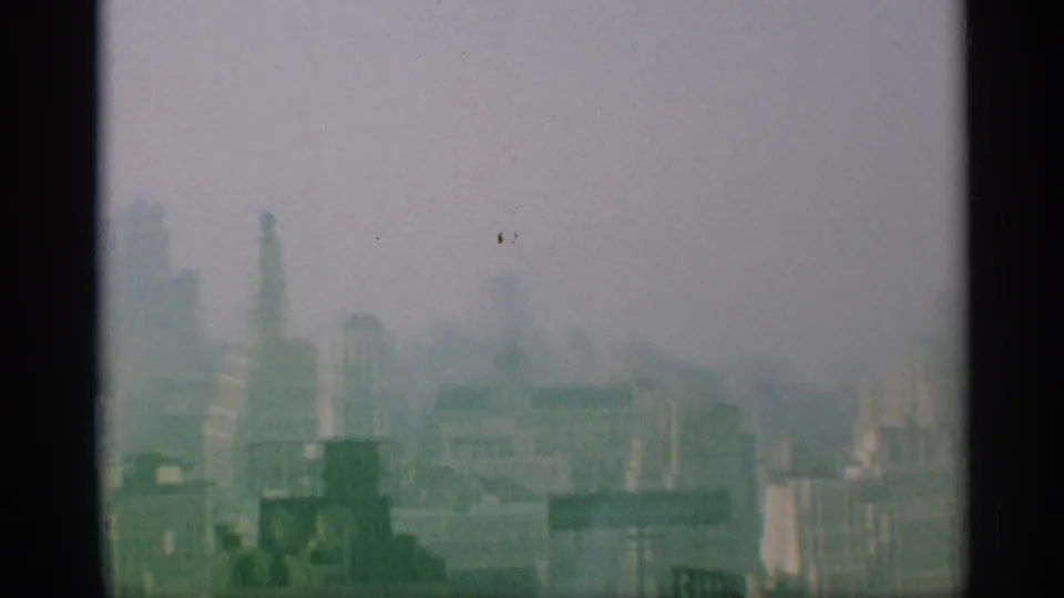 A hazy 1959 New York urban view shows tall towers and lower buildings softened by 8mm grain and exposure.