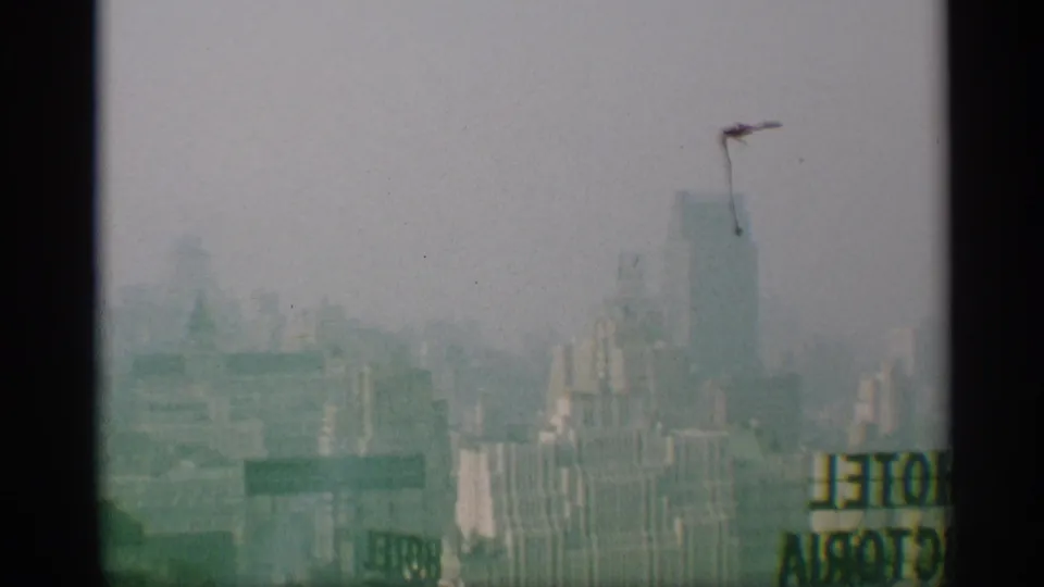 A mid-century New York skyline view includes a partial sign near the lower edge and a tall blocky building in haze.