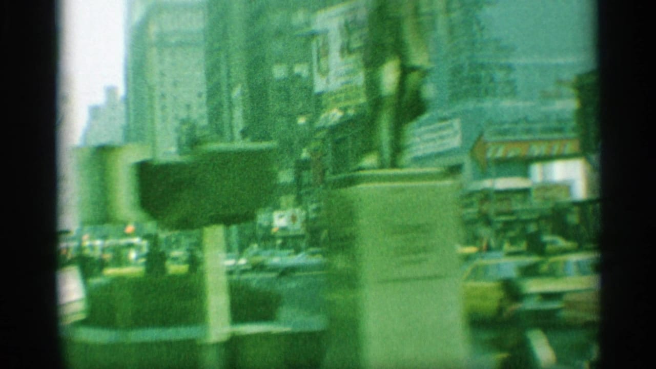 Street traffic and sidewalks framed by tall buildings, signs, and a foreground street fixture.