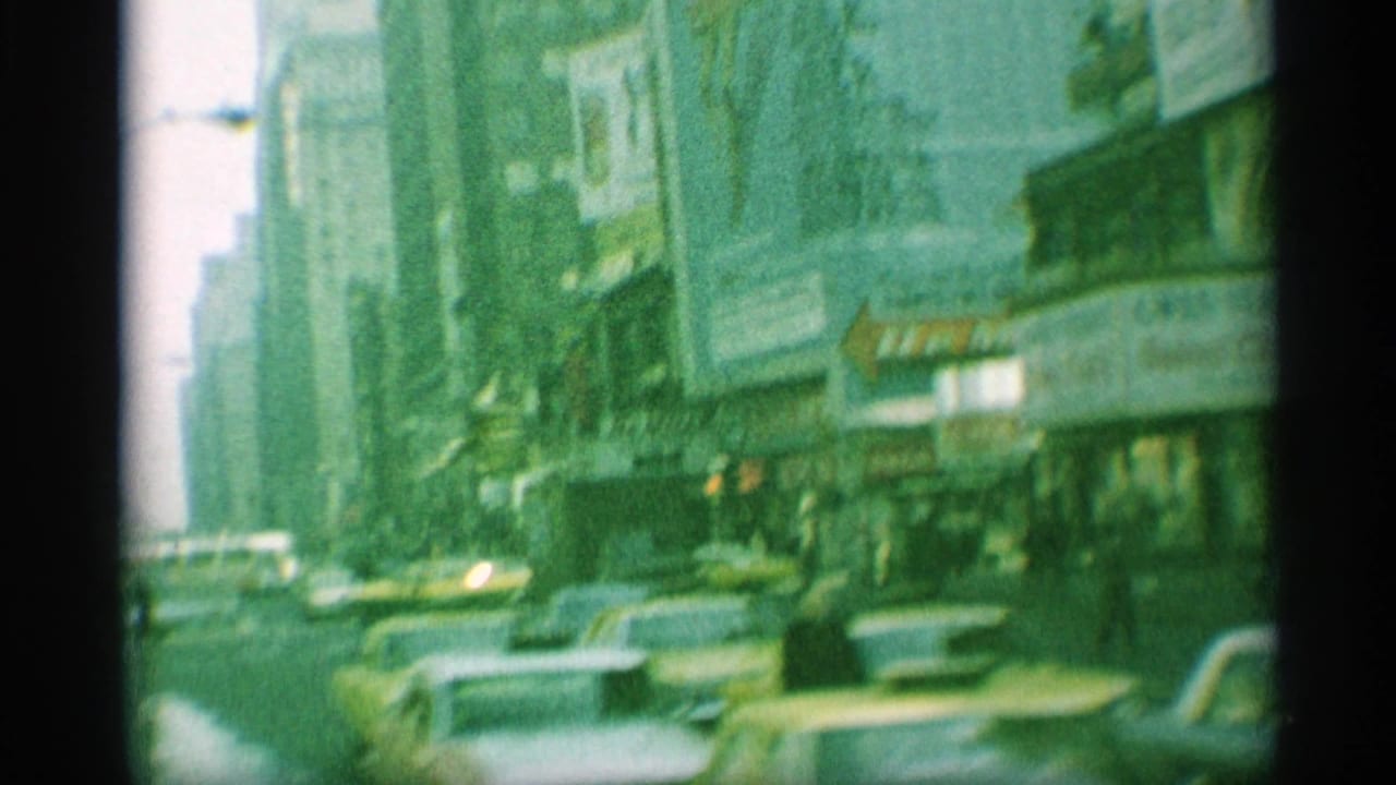 Green-tinted 8mm view of a 1959 New York street with yellow taxis, classic cars, sidewalk crowds, storefronts, and theater-style signs.