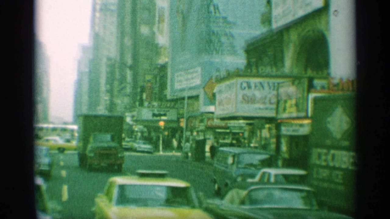 1959 New York street frame showing yellow cabs, traffic, pedestrians, tall buildings, billboards, and a theater marquee in vintage 8mm color.
