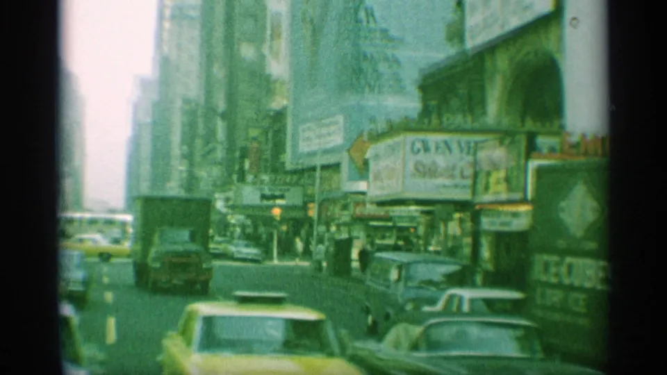 1959 New York street frame showing yellow cabs, traffic, pedestrians, tall buildings, billboards, and a theater marquee in vintage 8mm color.