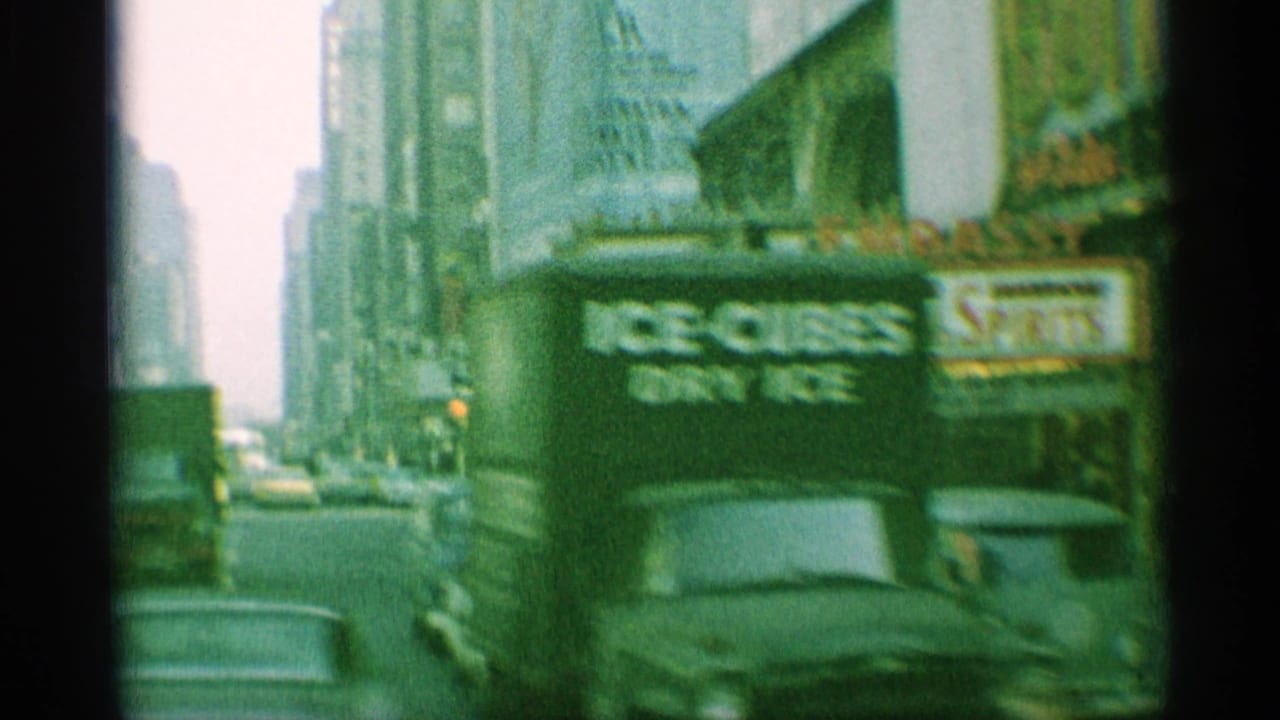 Downtown street with cars, storefront signs, pedestrians, and a theater marquee in soft green 8mm footage.