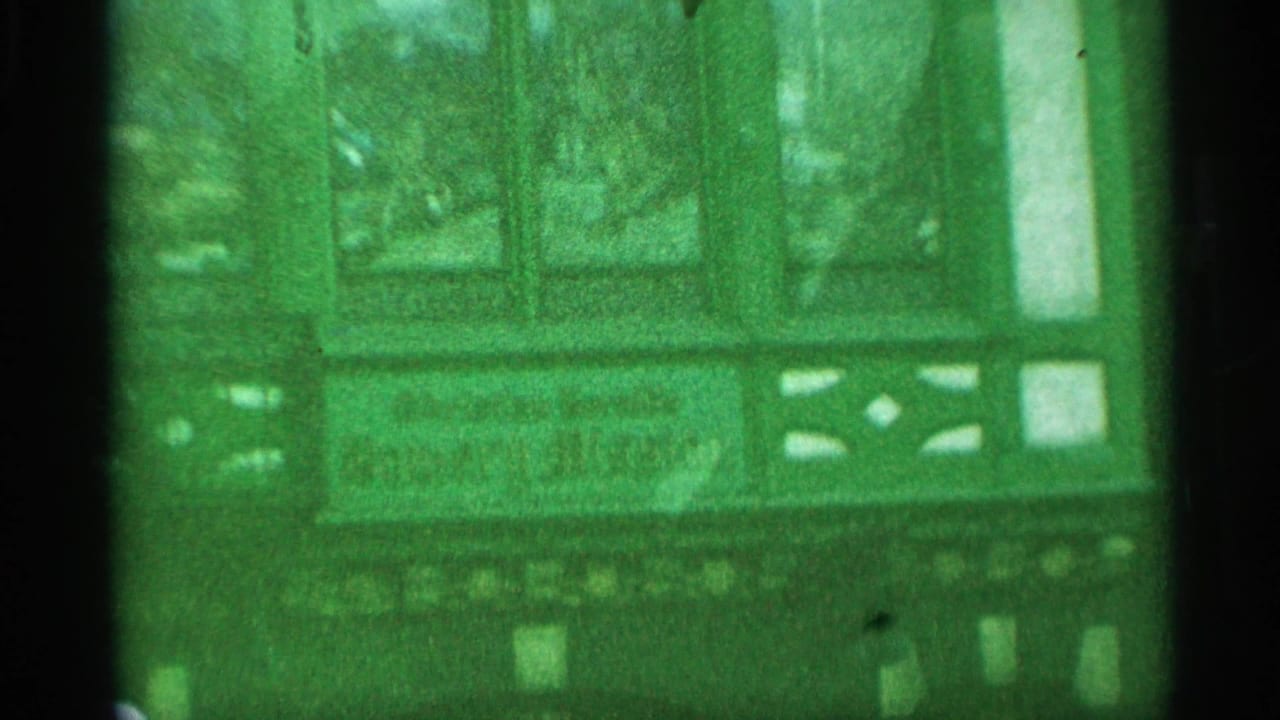 Handheld 1959 New York 8mm view of a theater entrance area with display cases, marquee details, and green color shift.