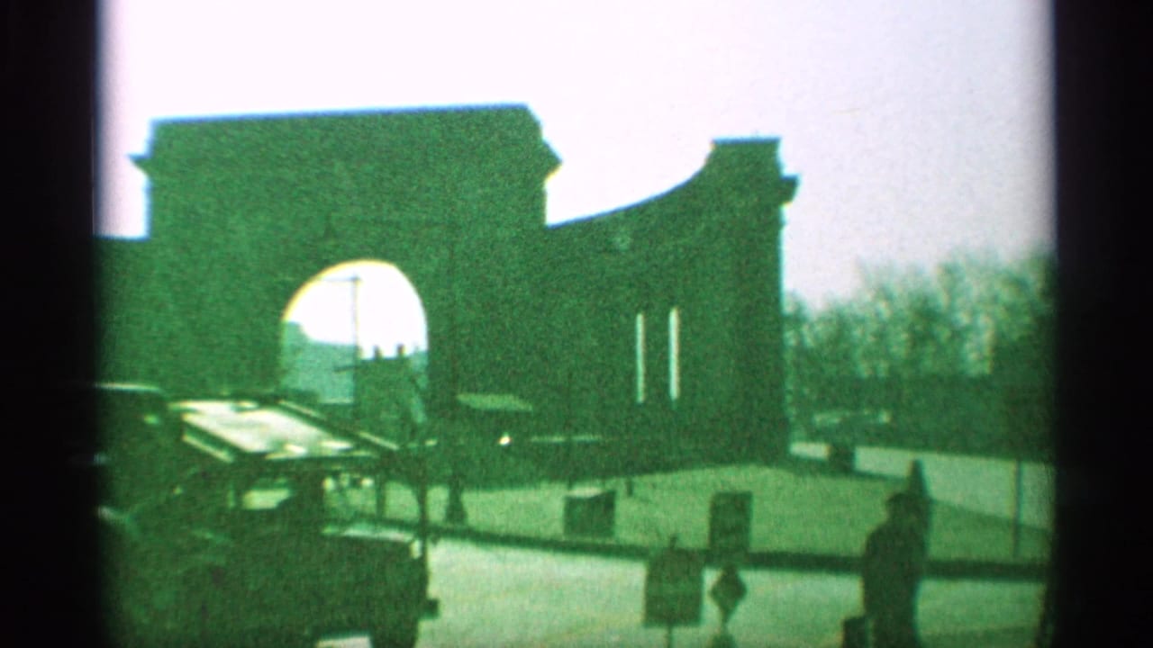 1959 New York street view with a large masonry archway, cars near the curb, and pedestrians in bright light.