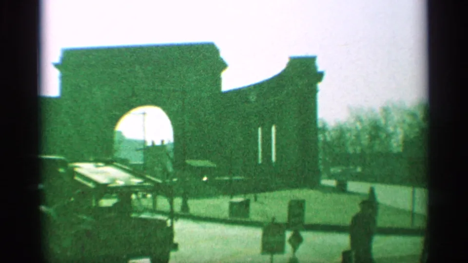 1959 New York street view with a large masonry archway, cars near the curb, and pedestrians in bright light.