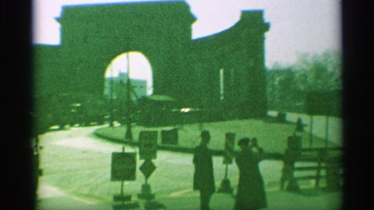 Green-tinted 1959 New York frame showing the archway, street signs, parked cars, and pedestrians near the curb.