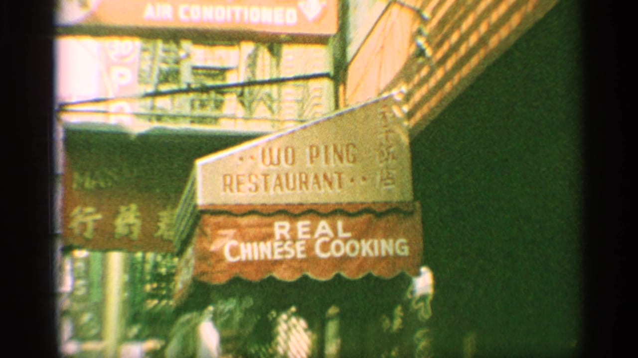 1959 New York street frame showing a Woo Ping Restaurant awning, Chinese signage, fire escapes, and pedestrians near the storefront.
