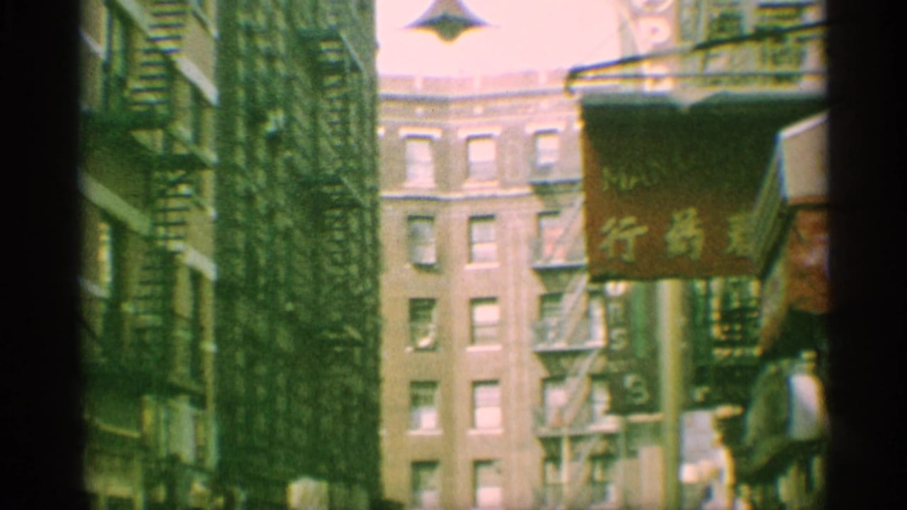 1959 New York street view with brick apartment facades, exterior fire escapes, a hanging Chinese-character sign, and storefront edges.