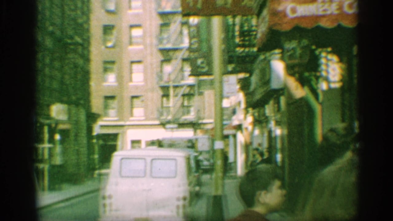 1959 New York street frame with a white van, brick buildings, fire escapes, shop awnings, and pedestrians near the sidewalk.