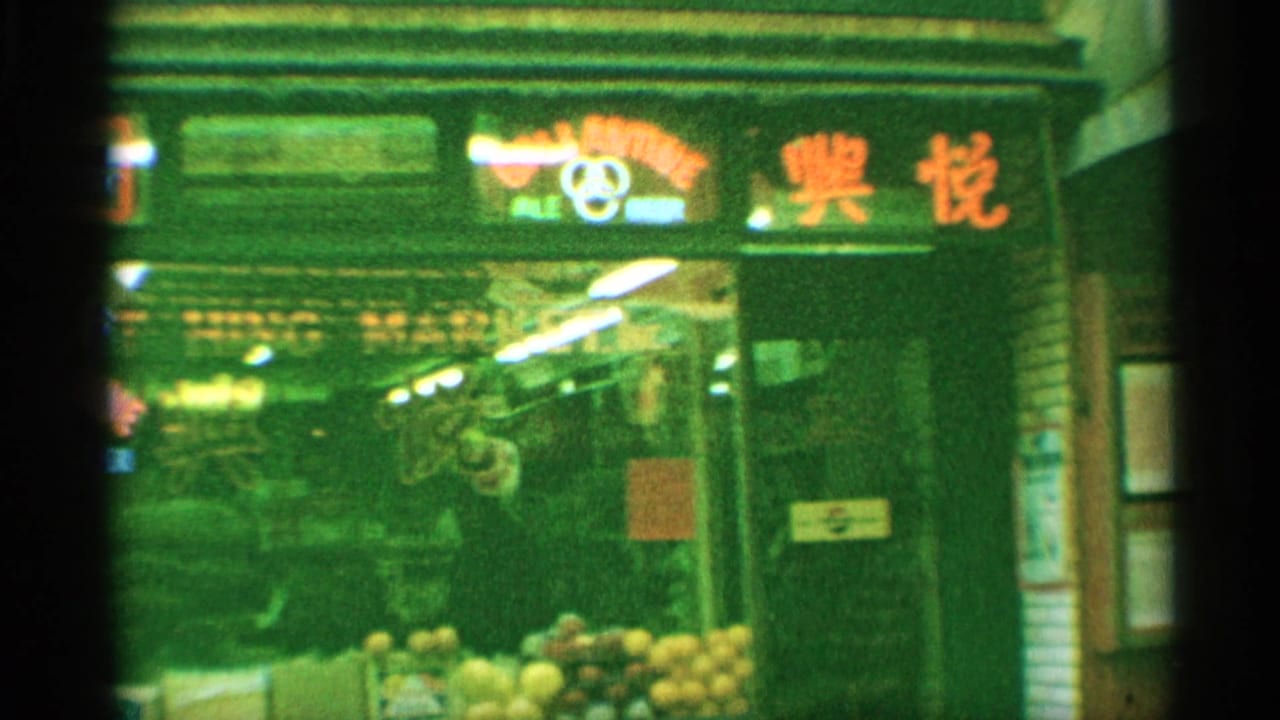 1959 New York night or low-light storefront view with neon signage, Chinese characters, produce or goods near the entrance, and pedestrians.