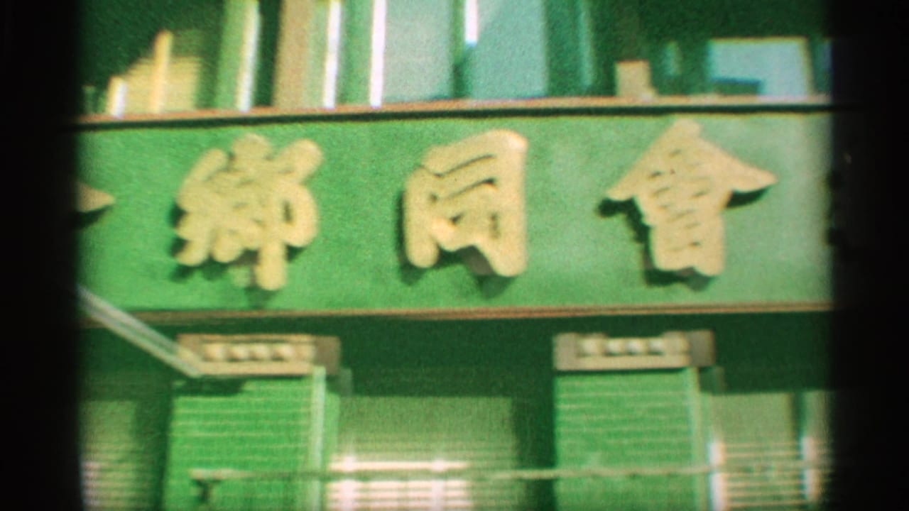 1959 New York 8mm frame focused on a green sign bearing gold Chinese characters above storefront windows.