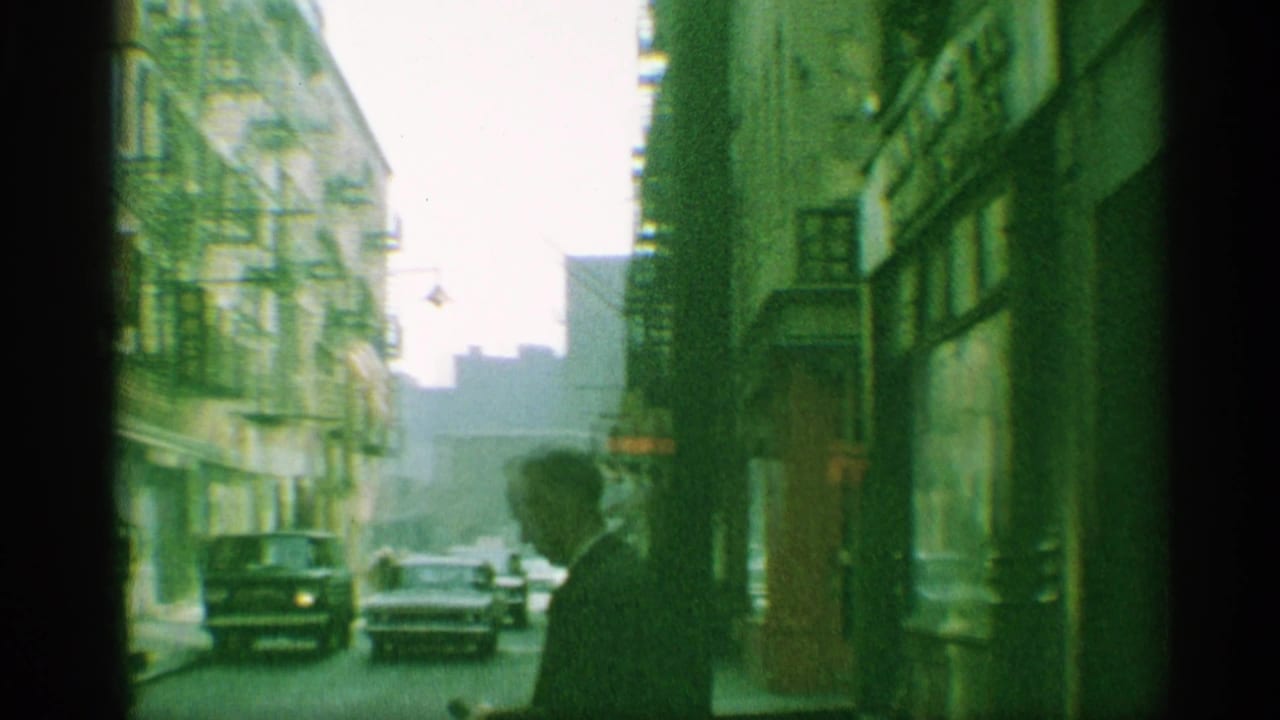 1959 New York street scene with a suited man in silhouette, passing cars, fire escapes, and storefront frontage.