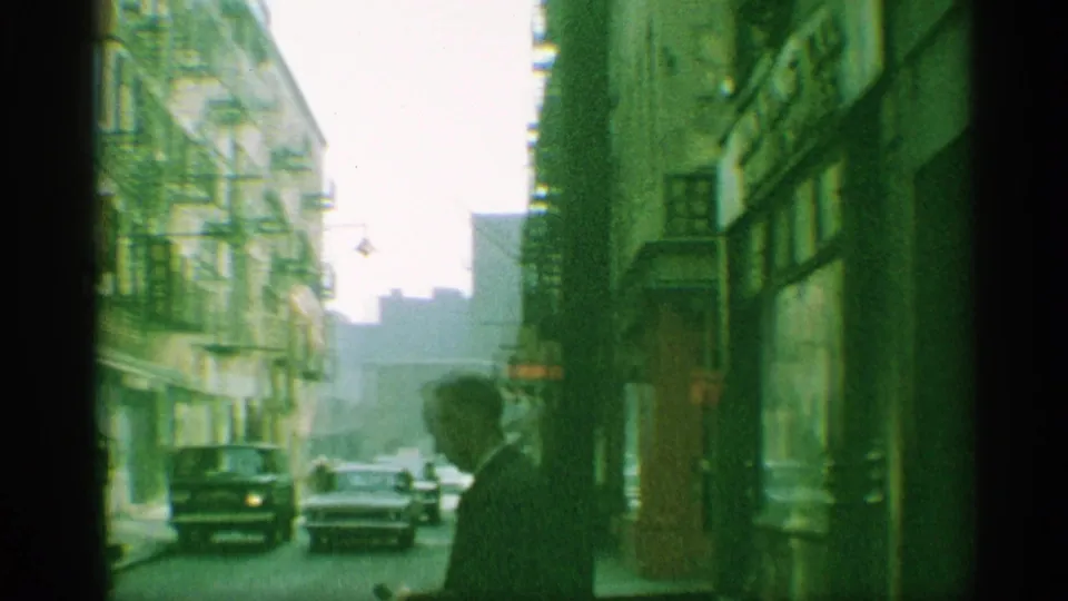 1959 New York street scene with a suited man in silhouette, passing cars, fire escapes, and storefront frontage.