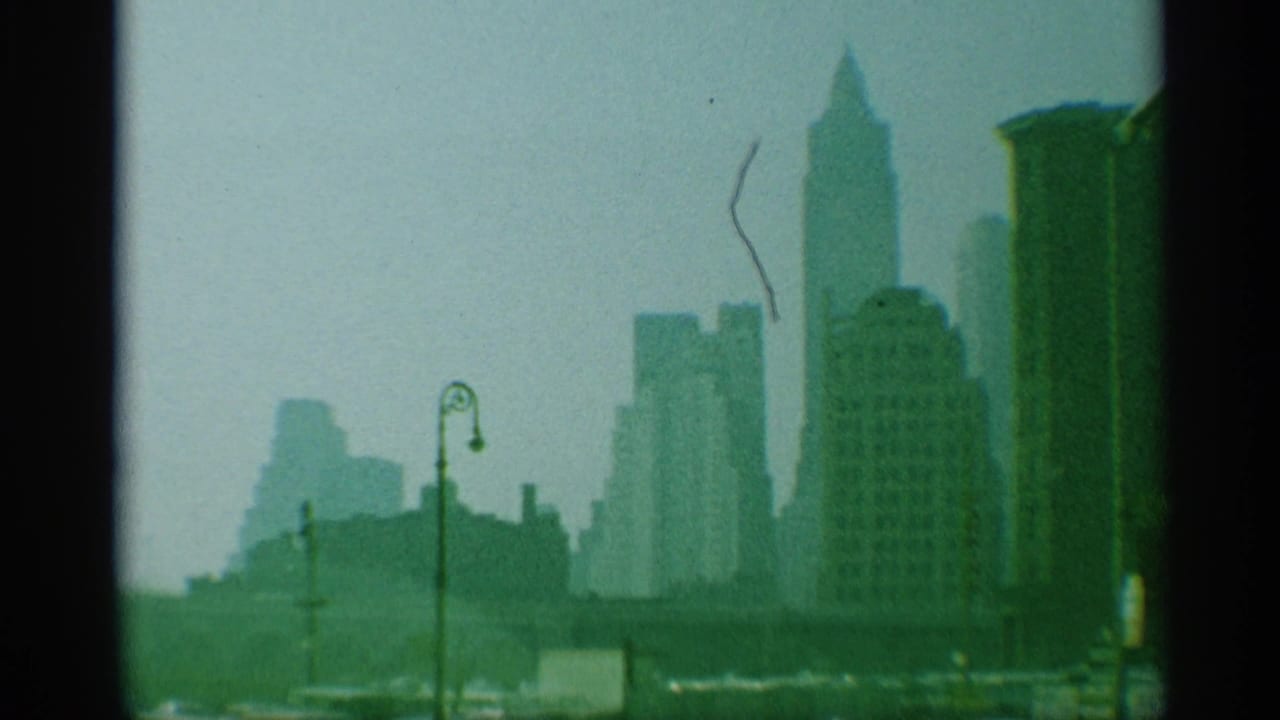 Hazy 1959 New York skyline view with tall buildings silhouetted beyond a street lamp and dark 8mm frame edges.