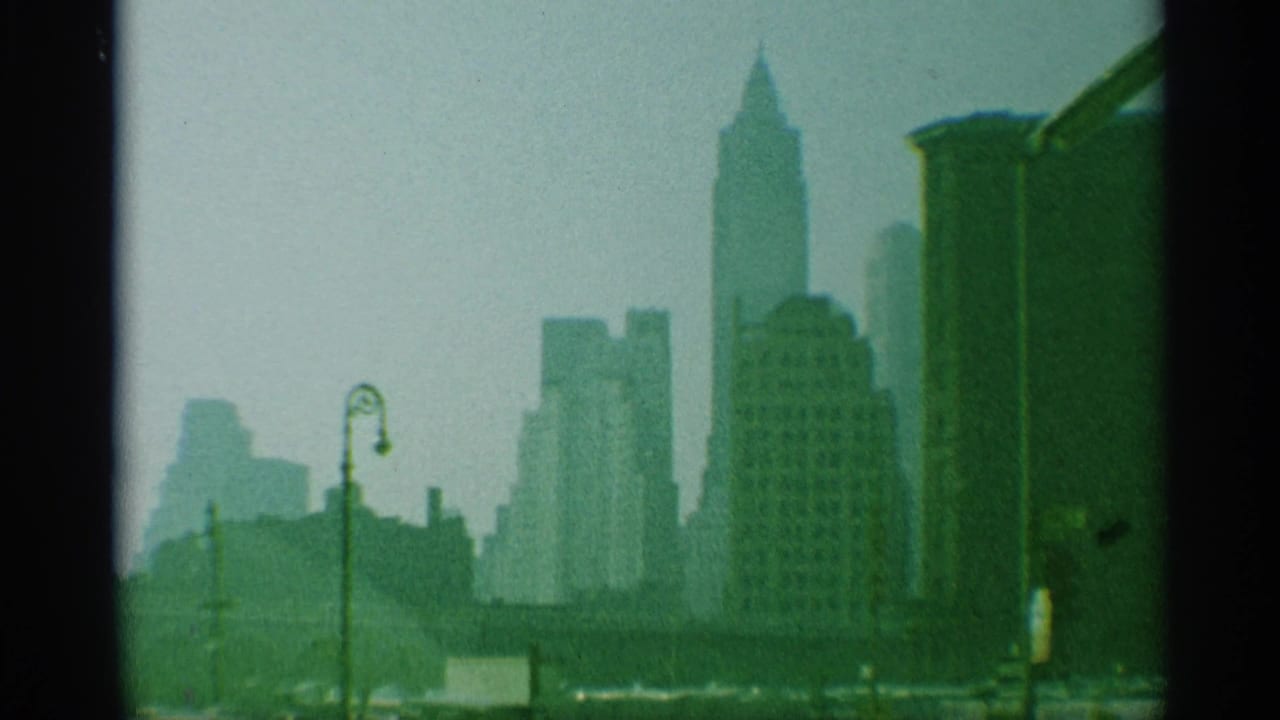 Green-tinted 8mm view of the New York skyline, with high-rises and a street lamp seen through haze.