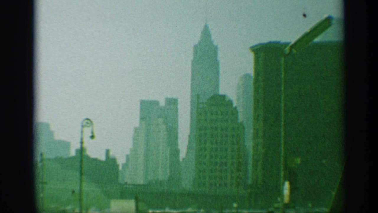 Late shot of the 1959 New York skyline, showing clustered towers, a foreground lamp, haze, and pronounced 8mm frame edges.