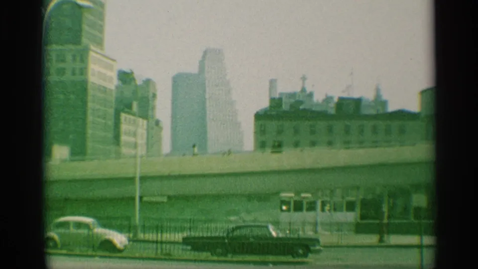 1959 New York cityscape with an elevated roadway, soft high-rises, fencing, and mid-century cars on the street below.