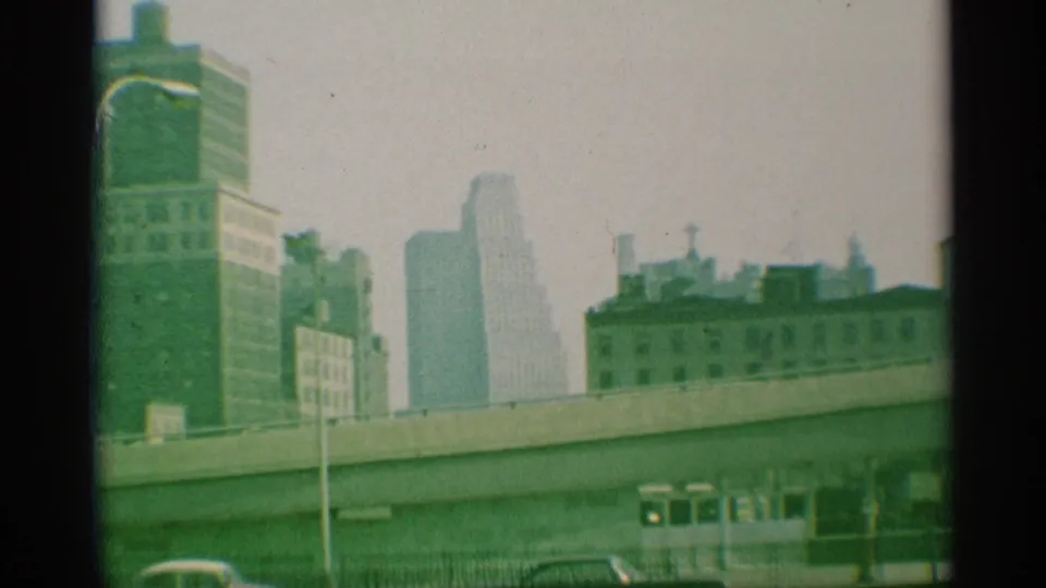 1959 New York street view with an elevated roadway, muted skyline, fence line, and mid-century cars below.