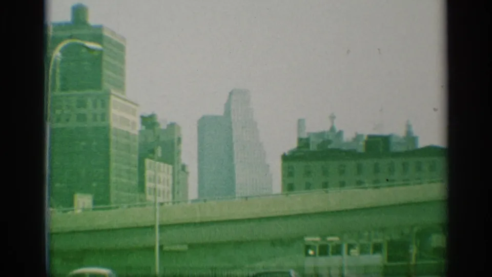 Wide 1959 New York cityscape showing elevated road infrastructure, muted high-rises, street fencing, and classic cars.