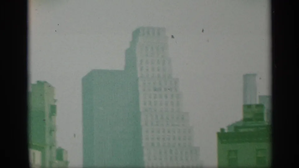 1959 8mm New York skyline with softened high-rises, pale sky, and dark vertical frame borders.