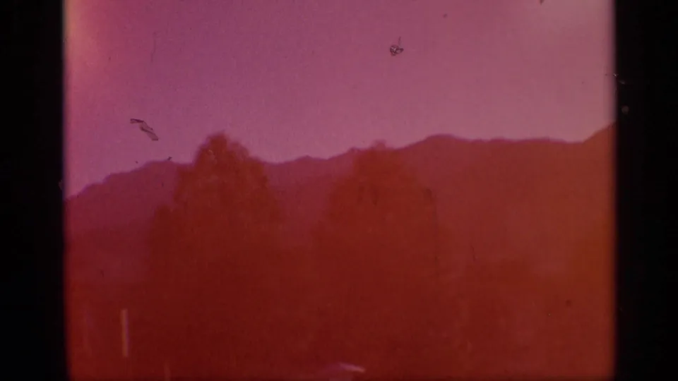 8mm mountain landscape view with silhouetted trees, low ridgeline, and strong reddish color shift.