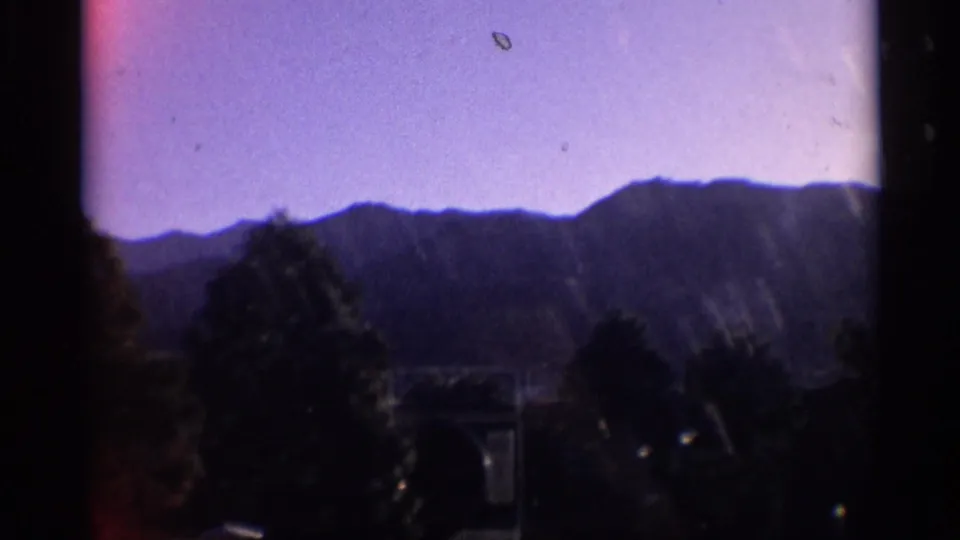 8mm mountain landscape with purple sky, silhouetted ridge, trees, and visible film wear.