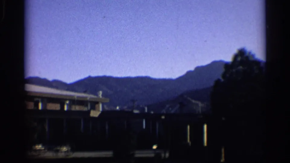 1959 New York 8mm view of a low suburban house, nearby tree, blue sky, and layered hills.