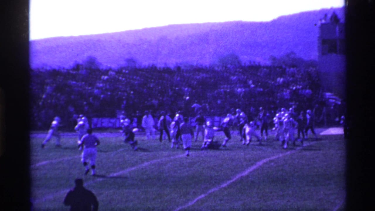 1969 Ohio 8mm frame showing a high school football play from a distant spectator angle, with players and a large sideline crowd visible.