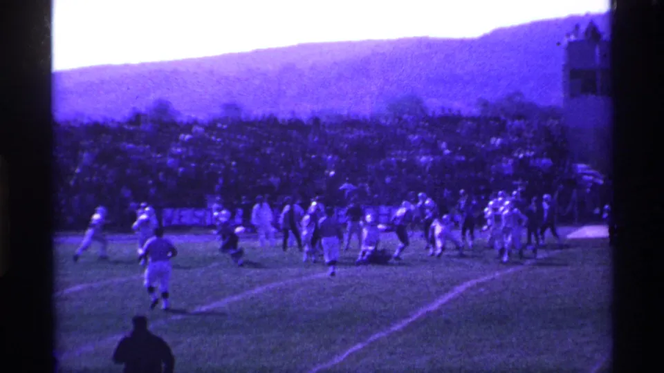 1969 Ohio 8mm frame showing a high school football play from a distant spectator angle, with players and a large sideline crowd visible.