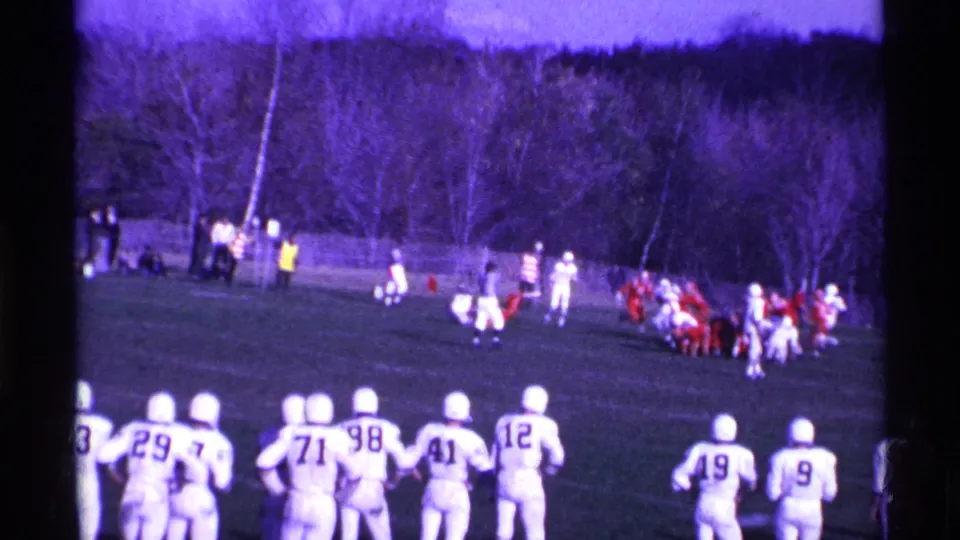 Sideline view of a 1969 Ohio football game, with numbered white jerseys in the foreground and red-uniformed players grouped farther away.