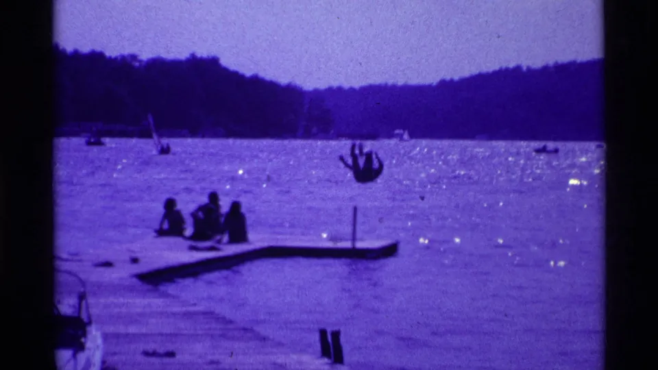 1969 Ohio lakeside frame showing a person upside down during a backflip from a dock as others watch from the water's edge.