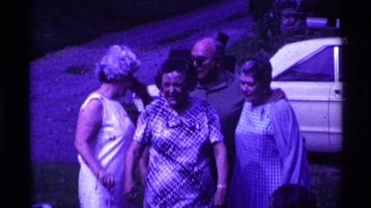 Four women and a man stand smiling outdoors, with a white car parked behind them.