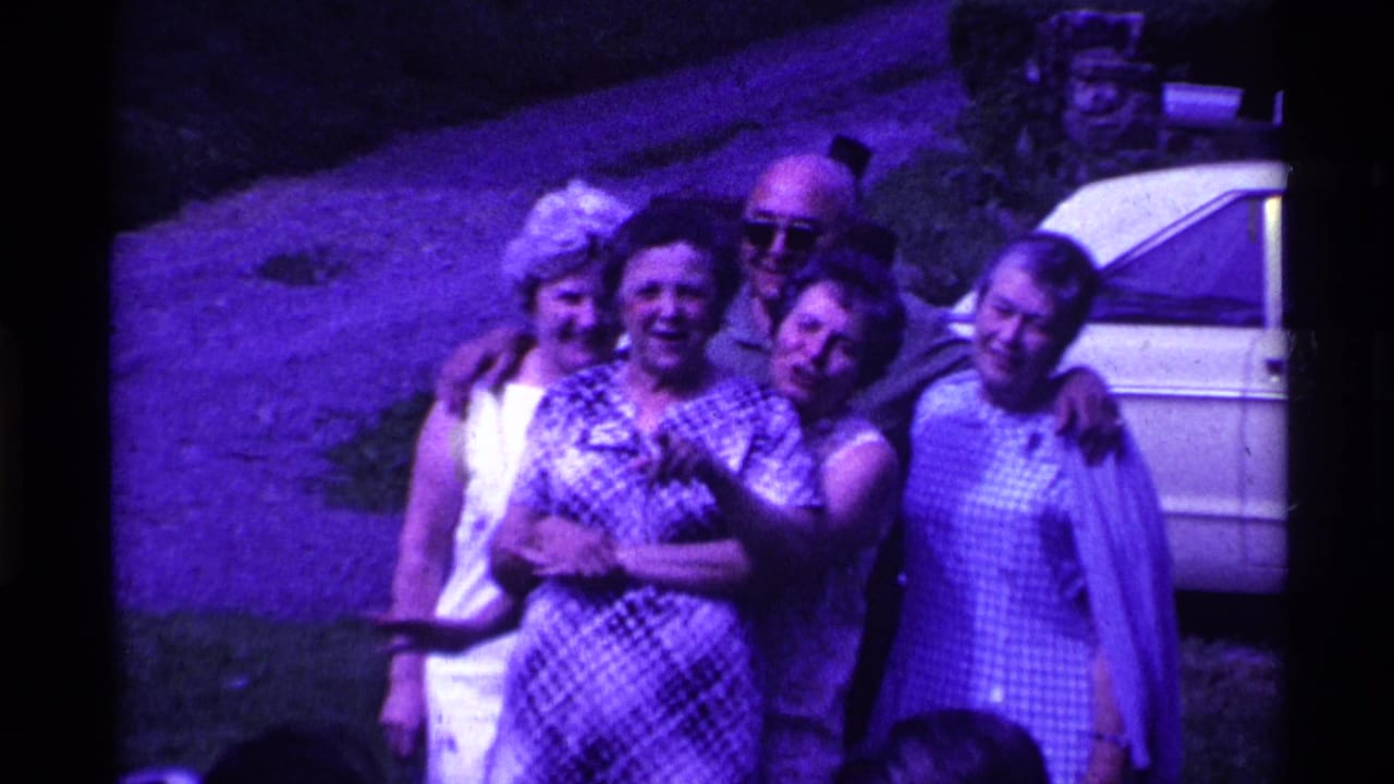 Adults pose together on a lawn near a parked car, with several women and a man in sunglasses.