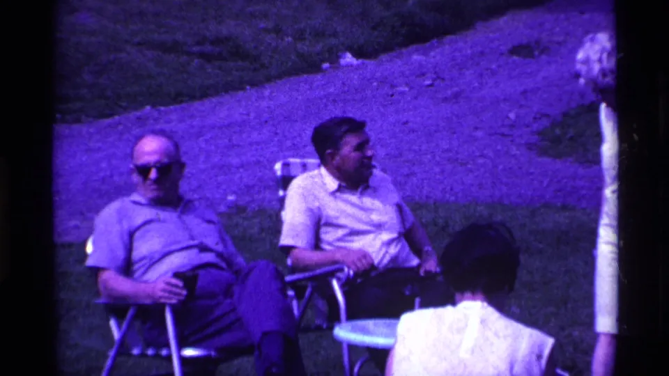Two men relax in folding lawn chairs during a 1969 Ohio outdoor gathering, with other adults nearby on the lawn.